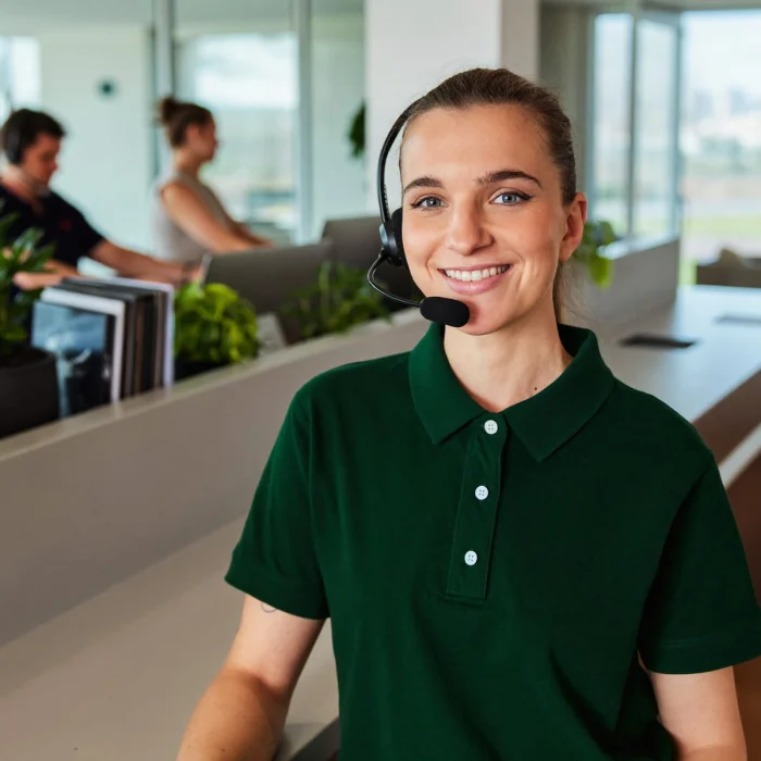 Een vriendelijke Glansco klantenservicemedewerker glimlacht met een headset op bij een lichte receptiebalie