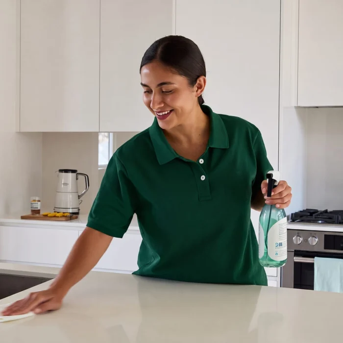 Een Glansco medewerker in een teal uniform veegt een modern keukenblad af met een milieuvriendelijke spray