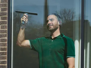 Een Glansco medewerker lapt een groot raam met een trekker